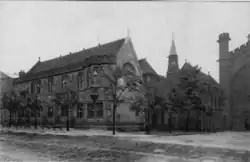 "Black and white photo of two storey mid-sized neo-gothic buildings next to the cathedral"